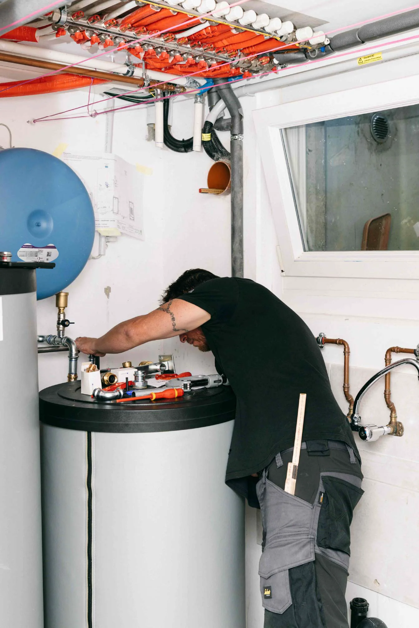 Personne intervenant sur un équipement cylindrique dans un local technique avec tuyaux et vannes visibles